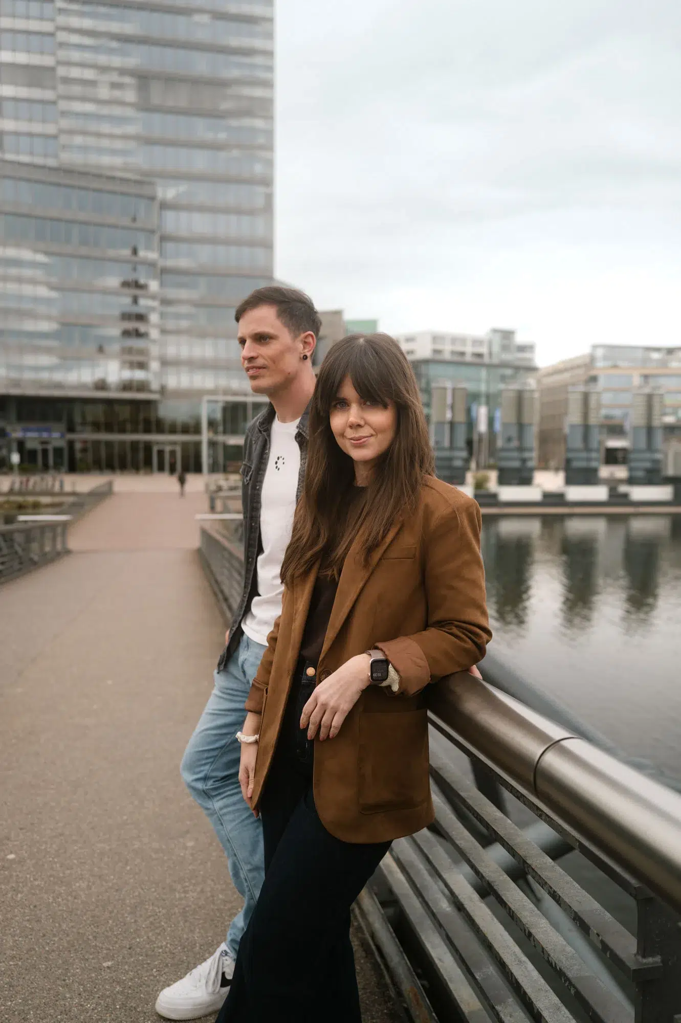 Viola und Steven Megerle lehnen an einem Geländer am Wasser, im Hintergrund moderne Gebäude